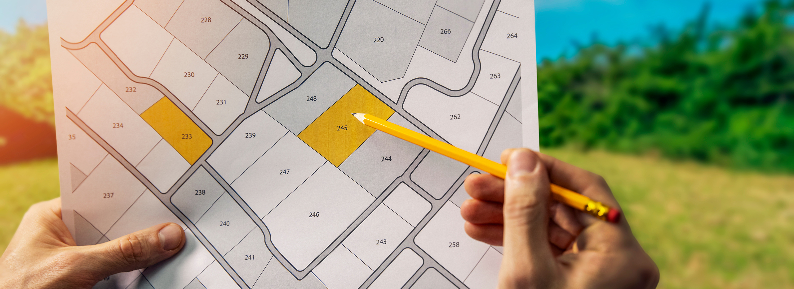 Hand zeigt mit Bleistift auf markiertes Baugrundstück in Flurkarte – Symbolbild für Grundstückssuche, Immobilienkauf und Bauplanung.