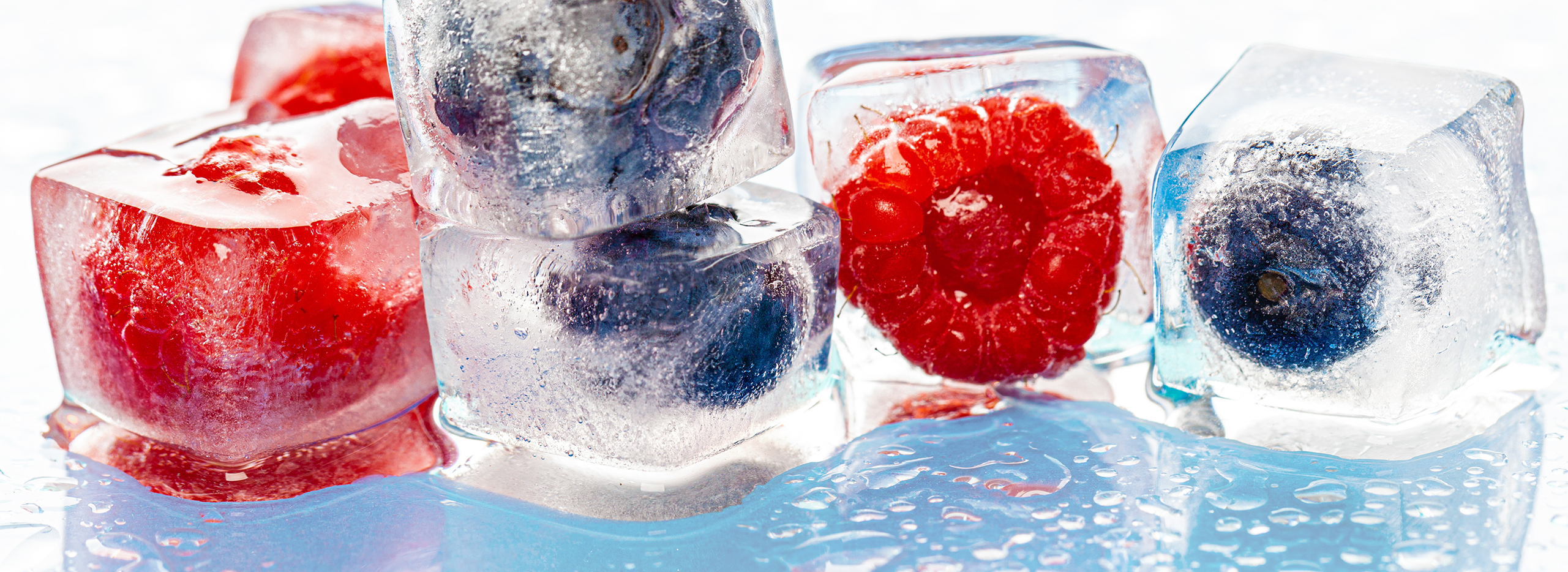 Kunstvoll gestaltete Eiswürfel mit eingefrorenen Himbeeren und Blaubeeren – eine kreative und erfrischende Idee.