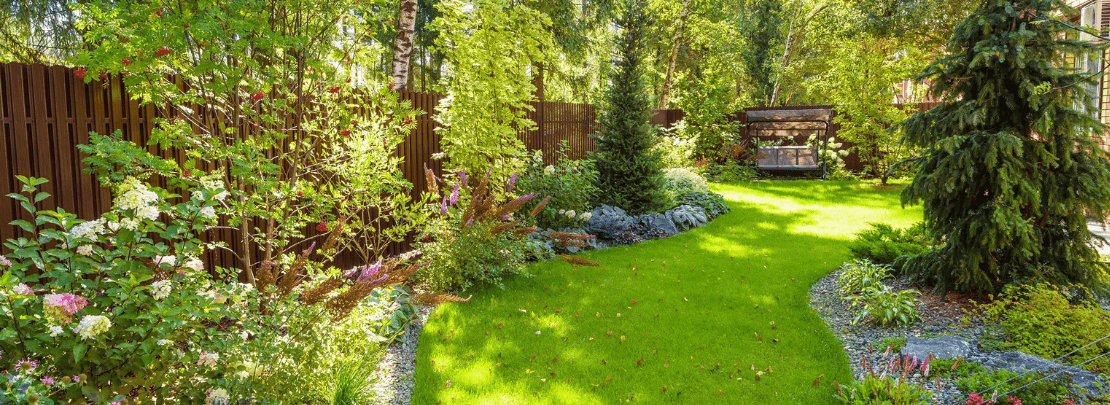 Gepflegten Naturgarten mit grünem Rasen, blühenden Sträuchern, Bäumen und gemütlicher Sitzgelegenheit