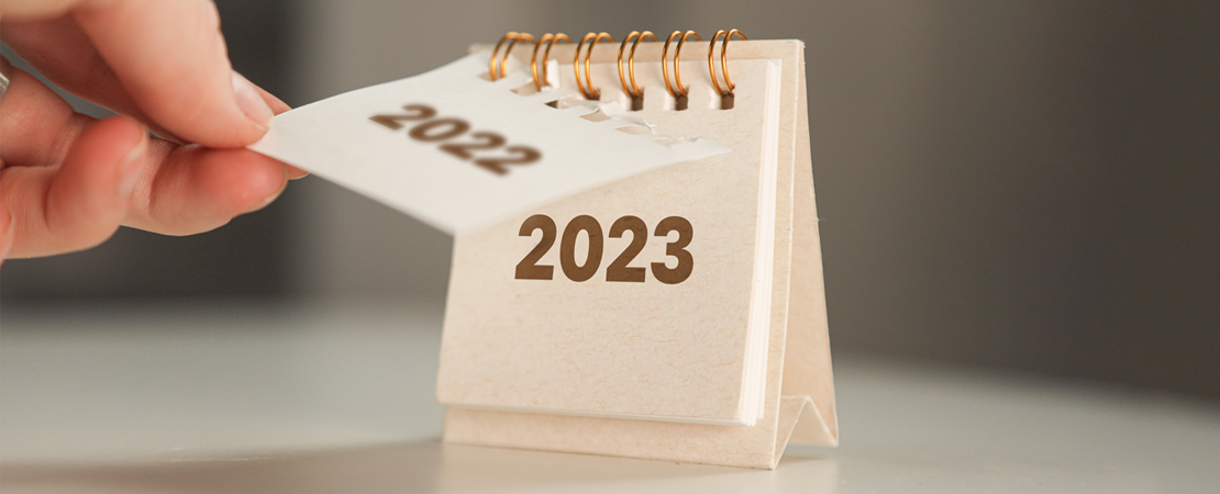 Hand blättert Tischkalender von 2022 auf 2023 um, symbolisiert Jahreswechsel und Änderungen.