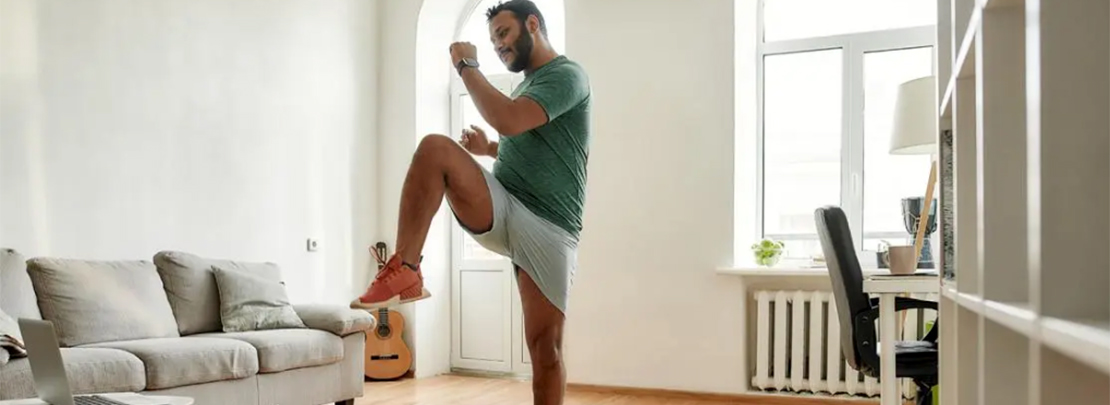 Mann macht Sportübung im Wohnzimmer vor dem Laptop für ein effektives Home-Workout. Doch ist Sport in der Wohnung erlaubt?