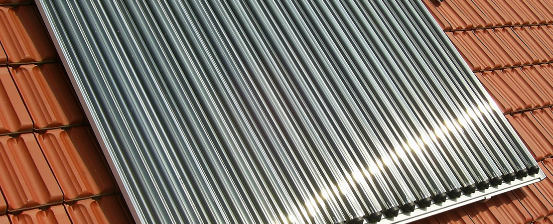 Solarkollektoren (Röhrenkollektoren) auf einem Ziegeldach in Nahaufnahme, die Sonnenlicht reflektieren. Die Röhren sind aus glänzendem Metall und gleichmäßig angeordnet.