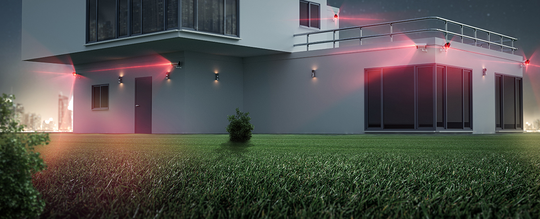 Modernes Wohnhaus bei Nacht mit aktivierter Außenüberwachung, dargestellt durch rote Laserlinien mehrerer Kameras und Bewegungssensoren. Symbolbild für Alarmanlage