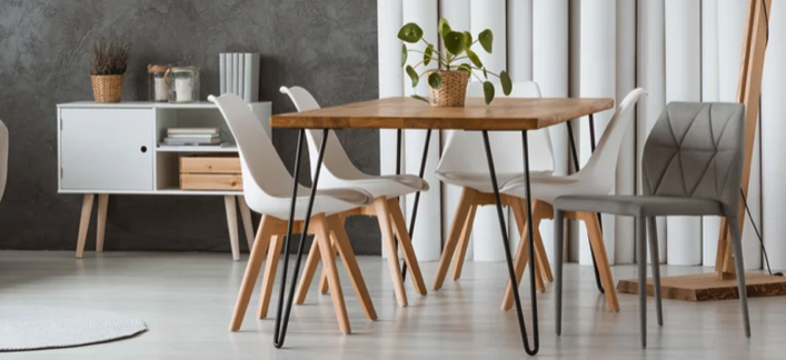 Skandinavisch eingerichtetes Esszimmer mit Holztisch, weißen und grauen Stühlen, Sideboard und dekorativer Zimmerpflanze.