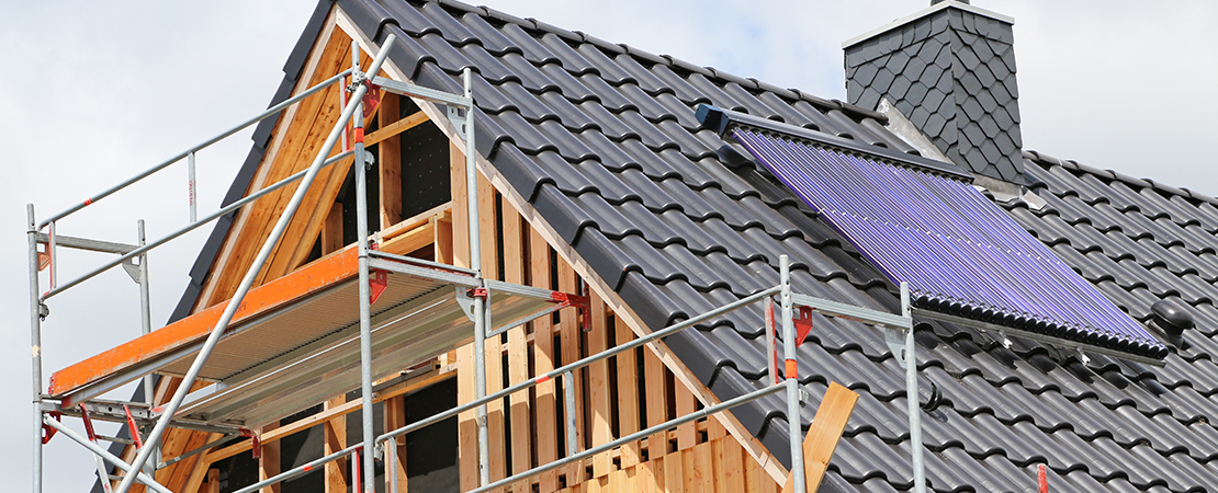 Ein Wohnhaus mit Baugerüst wird energetisch saniert, auf dem Dach ist eine Solaranlage installiert.