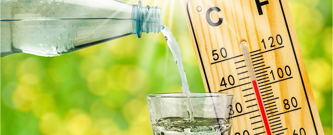 Eine Glasflasche gießt Wasser in ein Trinkglas, daneben zeigt ein Thermometer fast 40 Grad. Symbolbild für: Richtig essen und trinken bei Hitze.