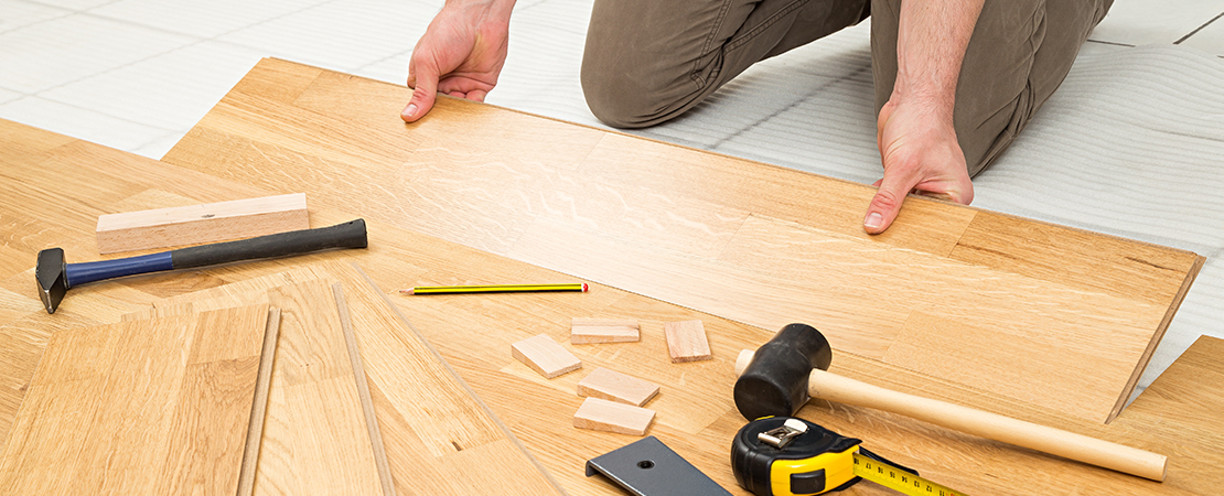 Verlegen von Laminat mit Hilfe von Hammer, Zollstock, Bleistift und Abstandskeilen.