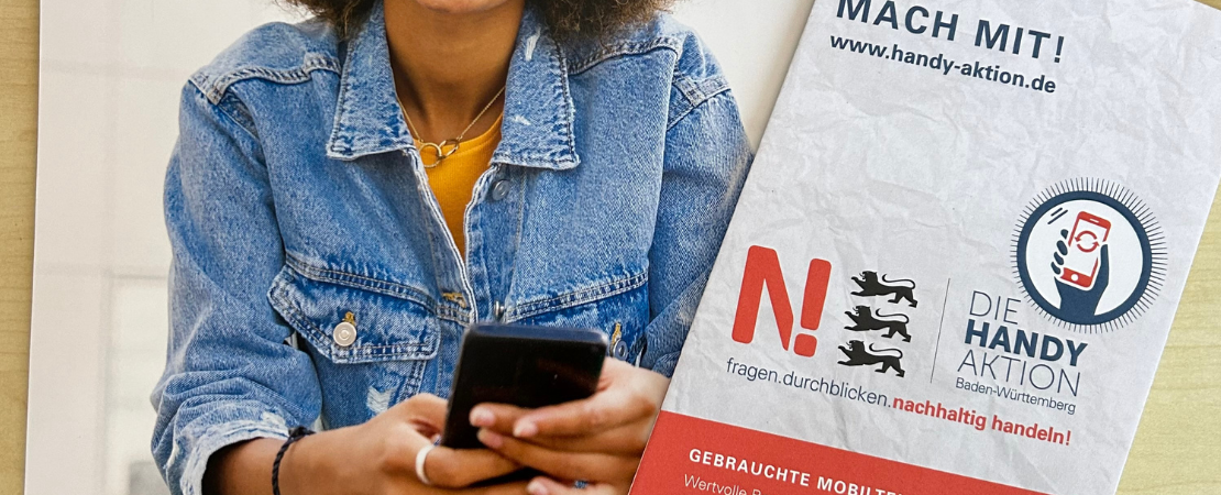 Eine Person in einer Jeansjacke hält ein Smartphone in der Hand. Daneben liegt ein Flyer der 'Handy-Aktion Baden-Württemberg' mit dem Slogan 'Fragen. Durchblicken. Nachhaltig handeln!' und einem Aufruf zur Teilnahme. Die Aktion setzt sich für das Recycling und die nachhaltige Nutzung von Mobiltelefonen ein.