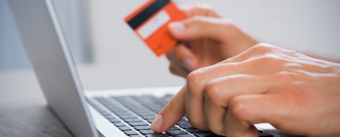Nahaufnahme einer Hand, die eine Kreditkarte hält, während die andere Hand auf einer Laptop-Tastatur tippt. Symbolbild für Online-Banking, digitale Zahlungsabwicklung und sicheres Online-Shopping.