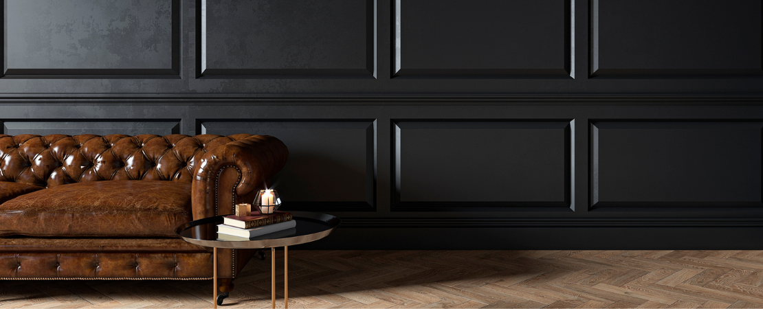 Luxuriös eingerichteter Raum mit einem klassischen Chesterfield-Ledersofa in Braun vor einer eleganten schwarzen Wand mit stilvollen Wandpaneelen schaffen eine gehobene Atmosphäre. Symbolbild für Exklusivität, Private Banking und hochwertige Finanzberatung.