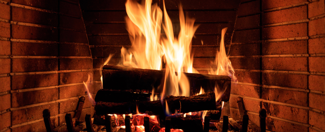 Nahaufnahme eines gemütlichen Kaminfeuers mit brennenden Holzscheiten in einem gemauerten Kamin. Die Flammen lodern und spenden warme, stimmungsvolle Beleuchtung. Symbolbild für Behaglichkeit, Wärme, Holzheizung und Entspannung am Kamin.